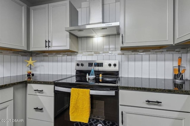 kitchen featuring stainless steel electric range oven, wall chimney range hood, dark stone countertops, and backsplash