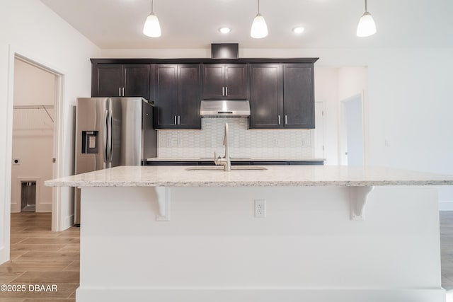 kitchen with a kitchen island with sink, hanging light fixtures, and light stone countertops