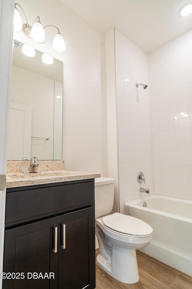 full bathroom with hardwood / wood-style flooring, tiled shower / bath, vanity, and toilet