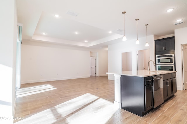 kitchen with a raised ceiling, a kitchen island with sink, pendant lighting, and stainless steel appliances