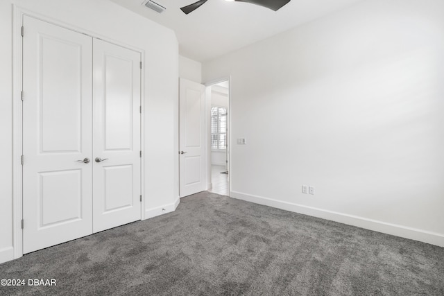 unfurnished bedroom with ceiling fan, a closet, and dark colored carpet