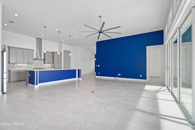 kitchen featuring gray cabinetry, backsplash, hanging light fixtures, wall chimney exhaust hood, and a center island