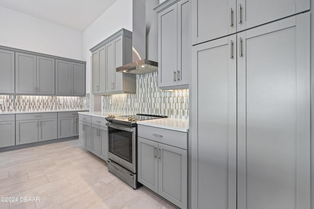 kitchen featuring wall chimney range hood, gray cabinetry, stainless steel range with electric stovetop, and tasteful backsplash