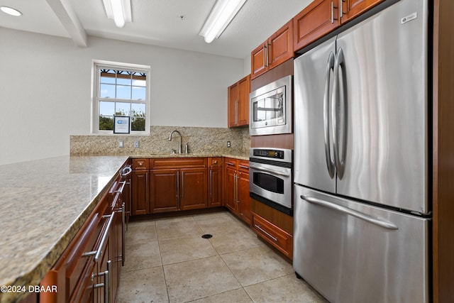 kitchen featuring stainless steel appliances, sink, kitchen peninsula, tasteful backsplash, and light stone countertops