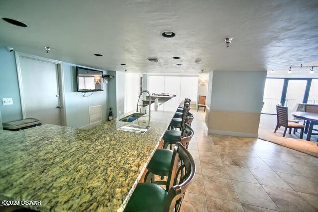 3757 S Atlantic Ave Unit 301, Daytona Beach Shores, FL 32118 - kitchen with a sink, white cabinetry, a kitchen breakfast bar, stone counters, and light tile patterned floors