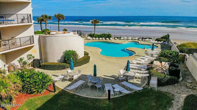 view of swimming pool featuring a patio, a water view, and a beach view