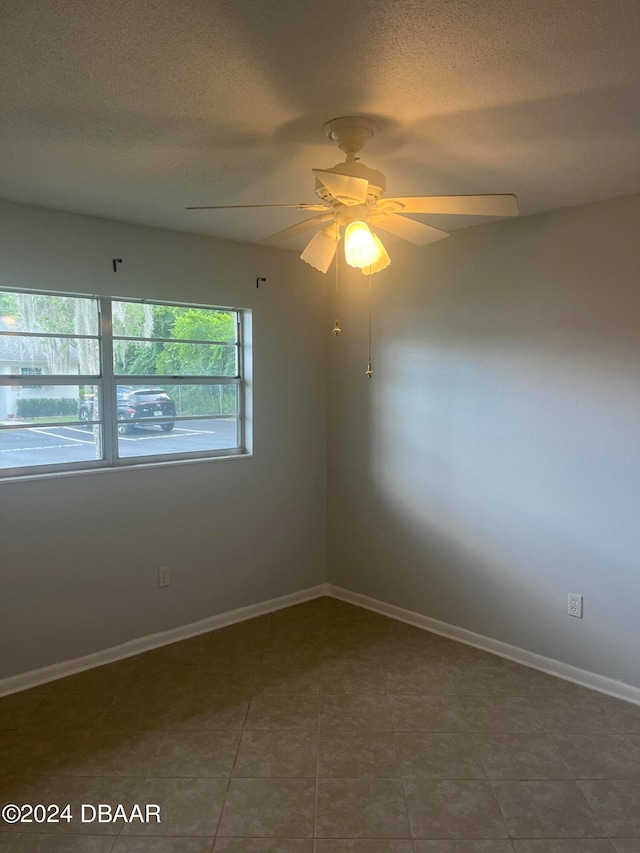 unfurnished room featuring a textured ceiling, dark tile patterned flooring, and ceiling fan