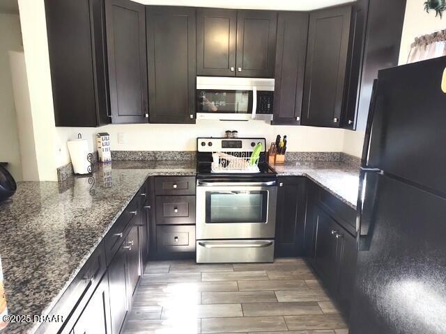 kitchen featuring dark brown cabinetry, stainless steel appliances, and dark stone counters