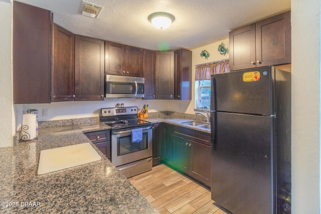 kitchen featuring dark countertops, light wood-style flooring, appliances with stainless steel finishes, a sink, and a textured ceiling