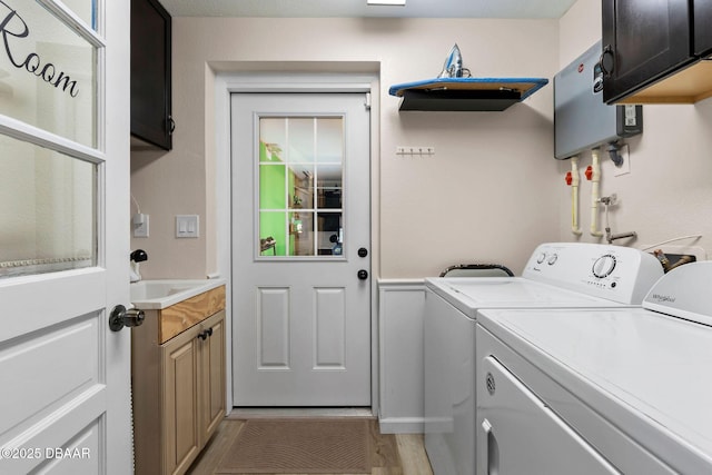 clothes washing area with water heater, sink, washing machine and dryer, and cabinets