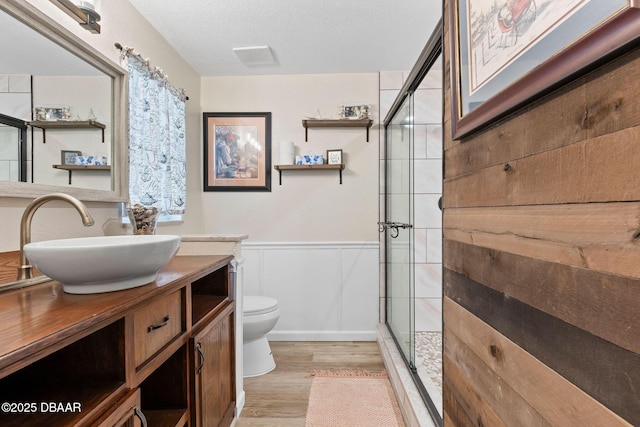 bathroom with a shower with door, hardwood / wood-style floors, vanity, a textured ceiling, and toilet