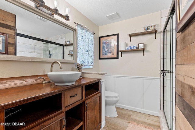 bathroom featuring hardwood / wood-style flooring, vanity, walk in shower, toilet, and a textured ceiling