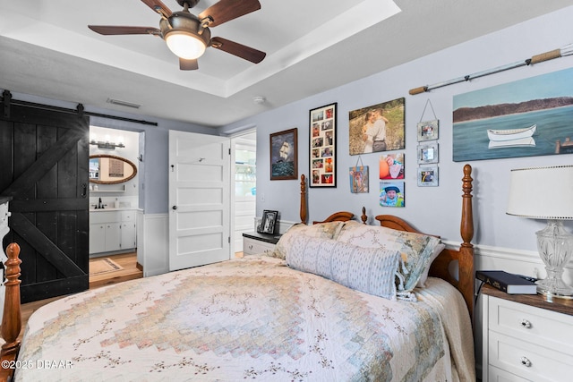 bedroom with ceiling fan, ensuite bath, a barn door, and a raised ceiling