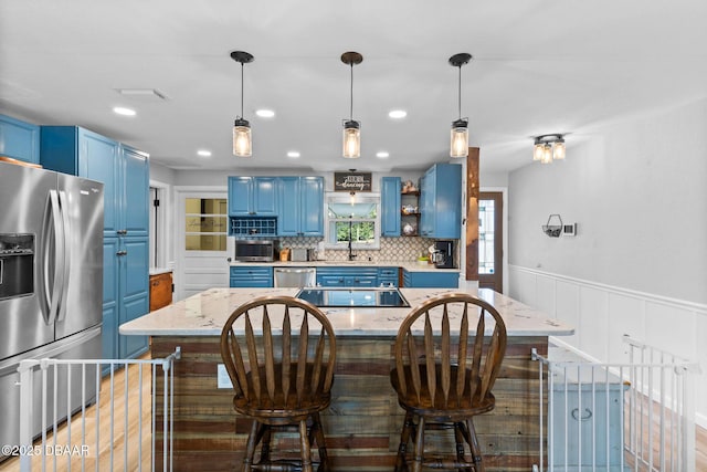 kitchen featuring blue cabinetry, stainless steel appliances, a center island, and light stone counters