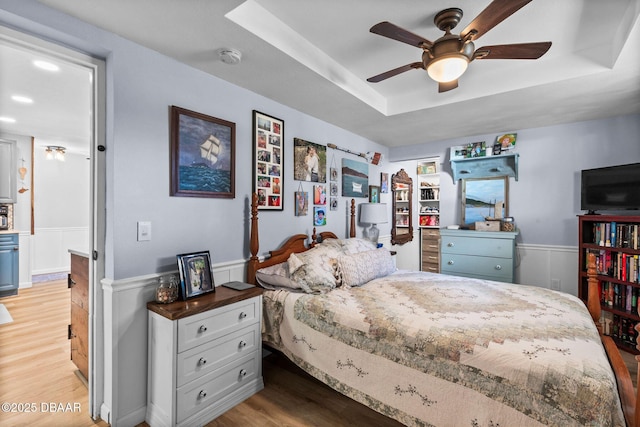 bedroom featuring a tray ceiling, ceiling fan, and light wood-type flooring