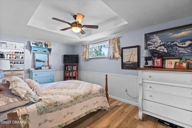 bedroom with a raised ceiling, ceiling fan, and light hardwood / wood-style flooring