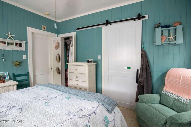 bedroom featuring wood walls, crown molding, tile patterned flooring, a barn door, and a closet