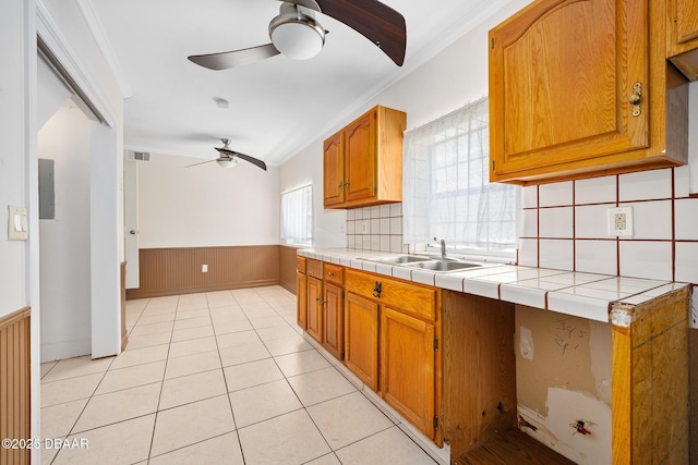 1650 Riverside Dr, Holly Hill, FL 32117 - kitchen with a ceiling fan, a wainscoted wall, brown cabinets, light tile patterned floors, and ornamental molding