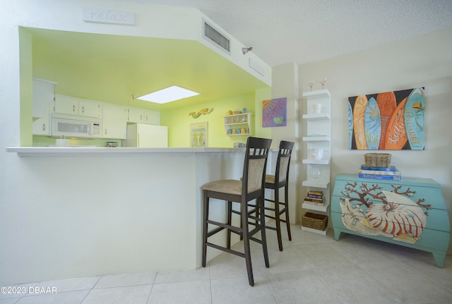 kitchen featuring white cabinetry, kitchen peninsula, light tile patterned floors, and white appliances