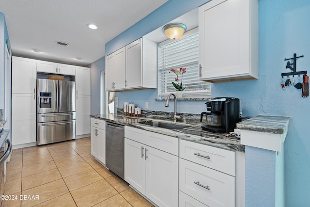 kitchen featuring dark stone counters, stainless steel appliances, sink, light tile patterned floors, and white cabinets