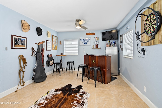 bar with stainless steel refrigerator, a wealth of natural light, ceiling fan, and light tile patterned floors