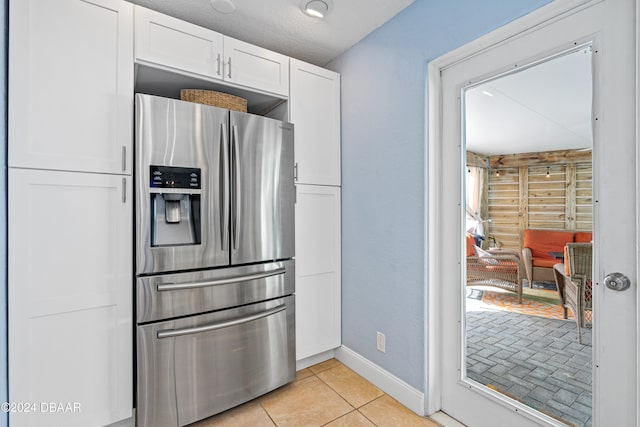 kitchen featuring stainless steel fridge with ice dispenser, light tile patterned floors, a textured ceiling, and white cabinetry