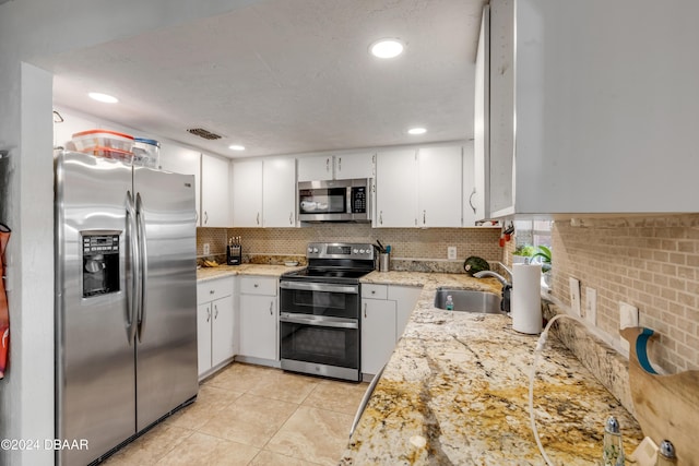 kitchen with light tile patterned flooring, stainless steel appliances, a sink, white cabinets, and backsplash