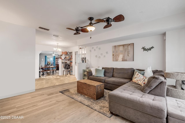 living room with light wood-type flooring, visible vents, and ceiling fan with notable chandelier