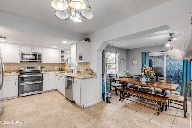 kitchen with tasteful backsplash, light stone counters, stainless steel appliances, white cabinetry, and a sink