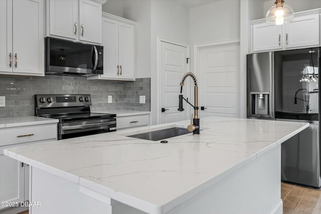 kitchen with decorative light fixtures, sink, white cabinets, stainless steel appliances, and a center island with sink