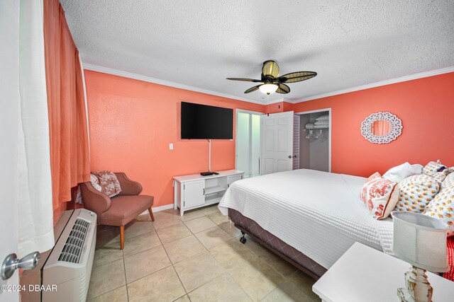 bedroom with a closet, light tile patterned flooring, ornamental molding, a textured ceiling, and ceiling fan