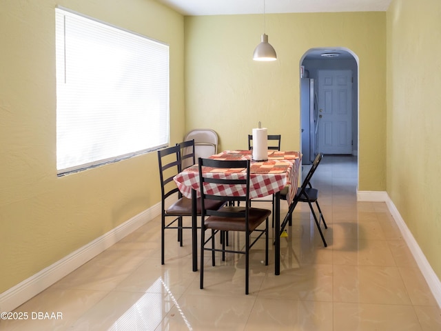 dining room with tile patterned floors, baseboards, and arched walkways