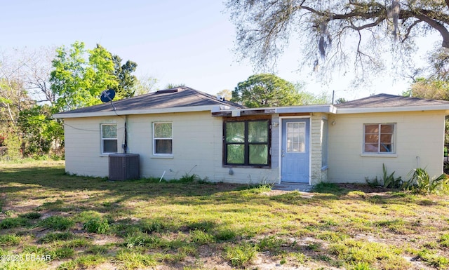 rear view of house with central air condition unit and a lawn