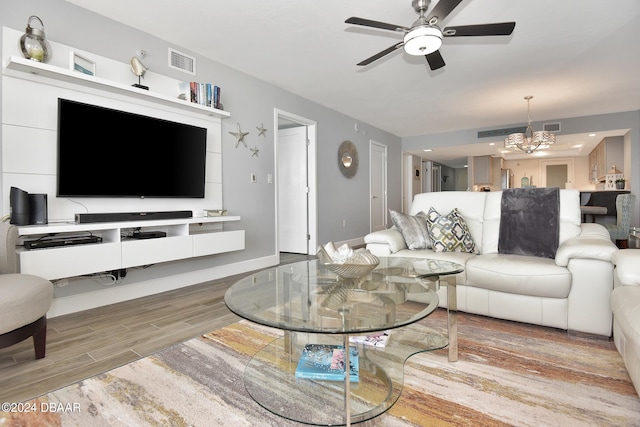 living room with ceiling fan with notable chandelier and light hardwood / wood-style flooring