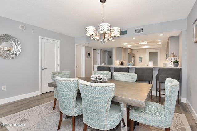 dining area featuring a chandelier, a raised ceiling, and light wood-type flooring