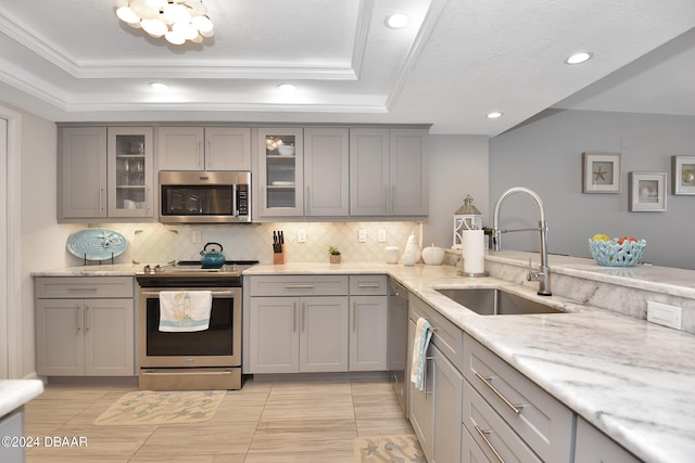 kitchen with sink, appliances with stainless steel finishes, light stone countertops, gray cabinets, and decorative backsplash