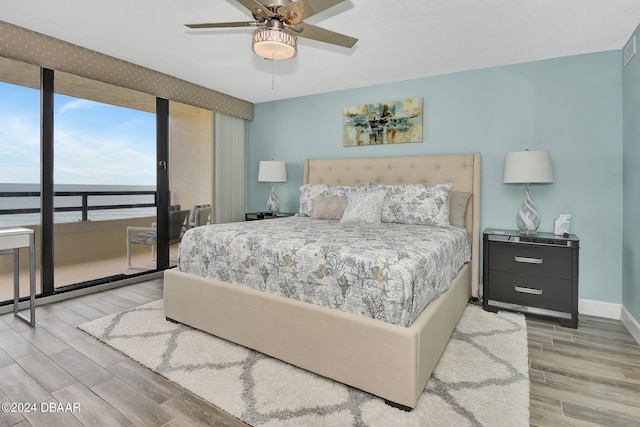 bedroom with hardwood / wood-style floors, ceiling fan, and a water view