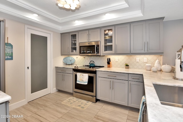 kitchen featuring gray cabinets, appliances with stainless steel finishes, crown molding, and a tray ceiling