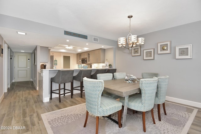 dining room featuring light hardwood / wood-style floors, a raised ceiling, and a notable chandelier