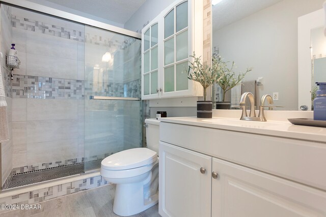 bathroom with toilet, hardwood / wood-style floors, a textured ceiling, vanity, and a shower with shower door