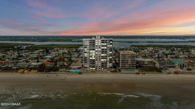 aerial view at dusk featuring a view of the beach and a water view