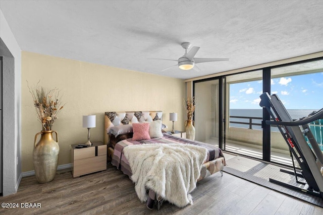 bedroom with hardwood / wood-style floors, access to outside, a water view, and ceiling fan