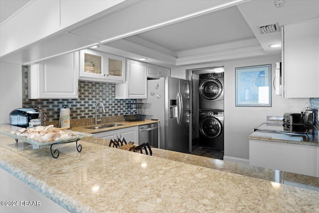 kitchen featuring stainless steel appliances, white cabinets, sink, a tray ceiling, and stacked washer / drying machine