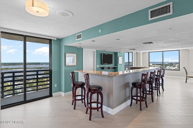 kitchen with expansive windows, plenty of natural light, light stone counters, and a breakfast bar