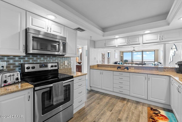 kitchen featuring stainless steel appliances, white cabinets, light wood-type flooring, and a tray ceiling