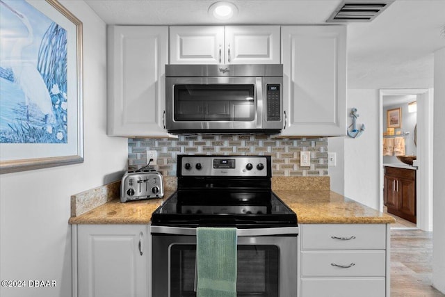 kitchen featuring light stone counters, appliances with stainless steel finishes, tasteful backsplash, light hardwood / wood-style flooring, and white cabinets