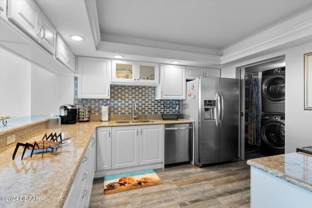 kitchen with white cabinetry, stainless steel appliances, sink, and stacked washer / dryer