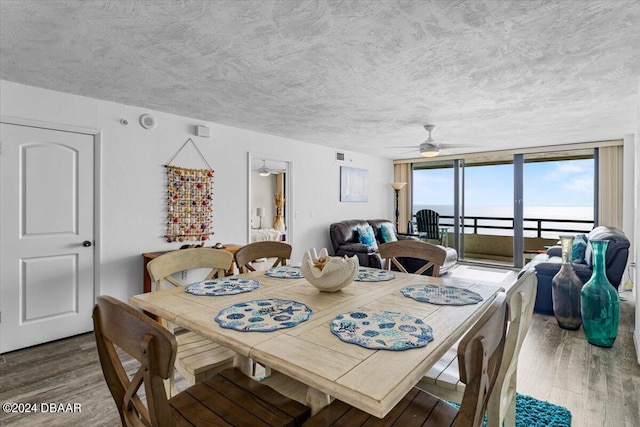 dining room featuring hardwood / wood-style flooring, a water view, ceiling fan, a textured ceiling, and expansive windows