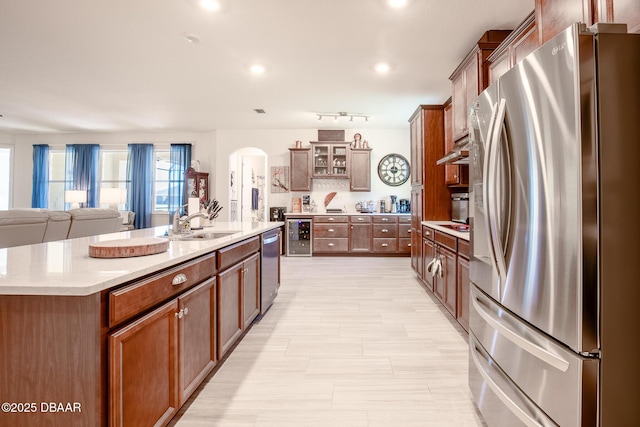 kitchen with sink, an island with sink, stainless steel appliances, and beverage cooler