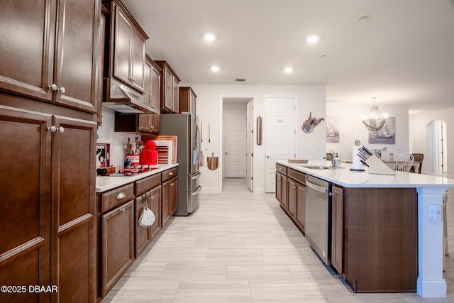 kitchen with appliances with stainless steel finishes, tasteful backsplash, decorative light fixtures, a notable chandelier, and an island with sink